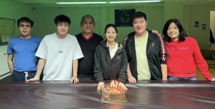Zhao, Yan, Victoria und andere Spieler der Akademie an einem Snookertisch, auf dem eine Geburtstagstorte steht.