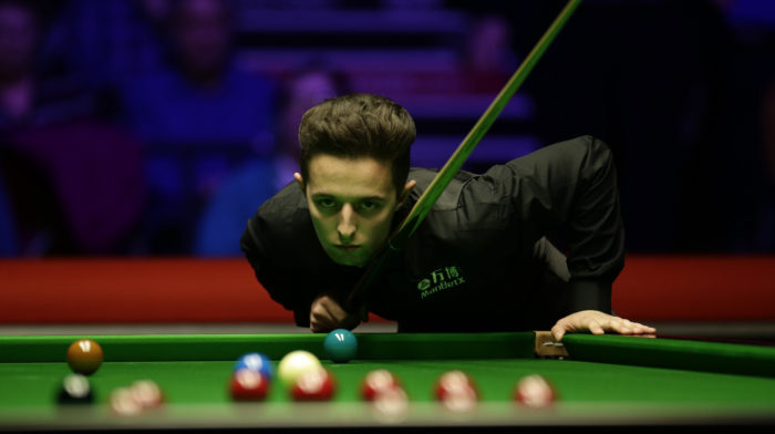 Joe O'Connor beugt sich über den Tisch und inspiziert kritisch die Winkel auf dem Tisch im Vordergrund. Am Publikum im Hintergrund erkennt man, dass es kein aktuelles Foto vom German Masters, sondern ein älteres Bild ist.