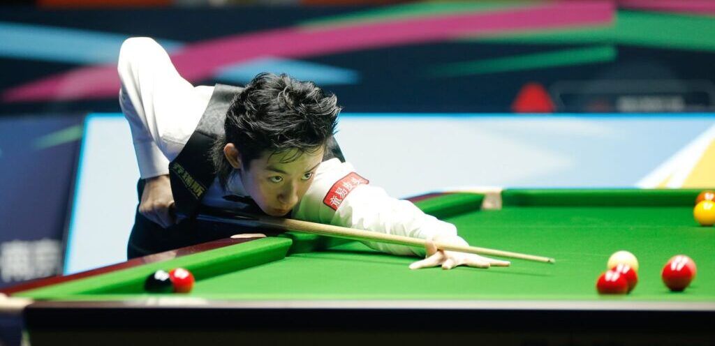 Wu Yize beim Stoß am Snookertisch. Er trägt einen verstrubbelten VoKuHiLa.