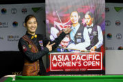 Mit strahlendem Lächeln zeigt Ploychompoo Laokiatphong auf ihr eigenes Bild auf dem Banner der Asia-Pacific Women’s Snooker Championship