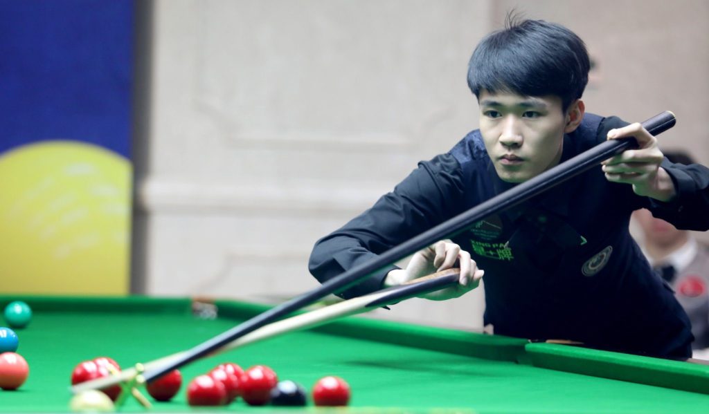 Junger chinesischer Spieler am Snookertisch. Er stößt gerade mit dem Hilfsqueue.
