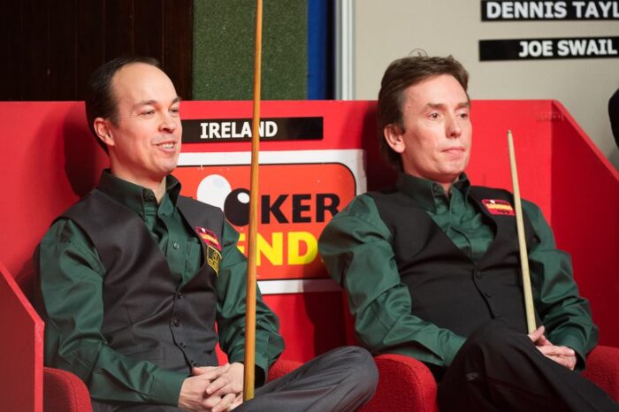 Fergal O'Brien und Ken Doherty sitzen nebeneinander in schwarzer Weste und dunkelgrünem Shirt mit ihrem Snookerqueue in der Hand. Hinter ihnen steht "Ireland". O'Brien lächelt und ist gut gelaunt.