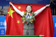 Weltmeisterin Bai Yulu mit üppigem Blumenkranz dekoriert hat ein breites Grinsen aufgesetzt und hält die chinesische Fahne hinter sich aufgespannt.
