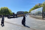 Ein Platz in Sheffield mit Bänken, einer langen Spiegelwand und einigen Menschen.