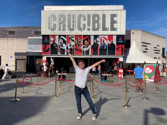Ein weißer Mann mittleren Alters posiert mit erhobenen Armen vor dem Crucible Theatre in Sheffield.