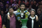 Wu Yize beim Pokalfoto, die Arme um die Schultern seiner Eltern rechts und links gelegt. Vor ihm der Pokal in Form einer großen, grauen Vase.