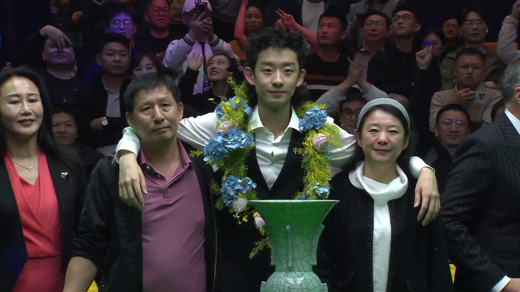 Wu Yize beim Pokalfoto, die Arme um die Schultern seiner Eltern rechts und links gelegt. Vor ihm der Pokal in Form einer großen, grauen Vase.