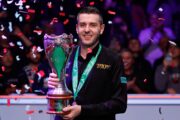 Mark Selby hält lächelnd die Trophäe der UK Championship, während Konfetti auf ihn herunterregnet.