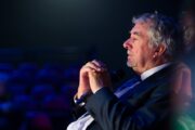 John Virgo im Profil bei einem Seniors-Event. Er sitzt ruhig und hat die Hände vor der Brust gefaltet.