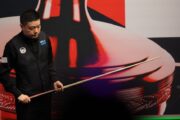 Ding Junhui steht mit seinem Queue im Crucible am Tisch vor der Trennwand und guckt auf den Tisch. Saudi