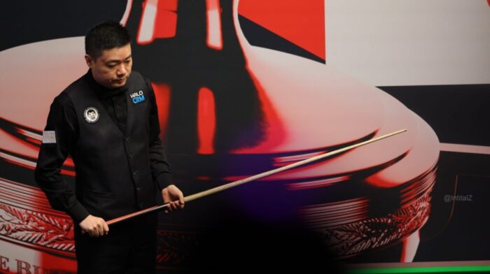 Ding Junhui steht mit seinem Queue im Crucible am Tisch vor der Trennwand und guckt auf den Tisch. Saudi