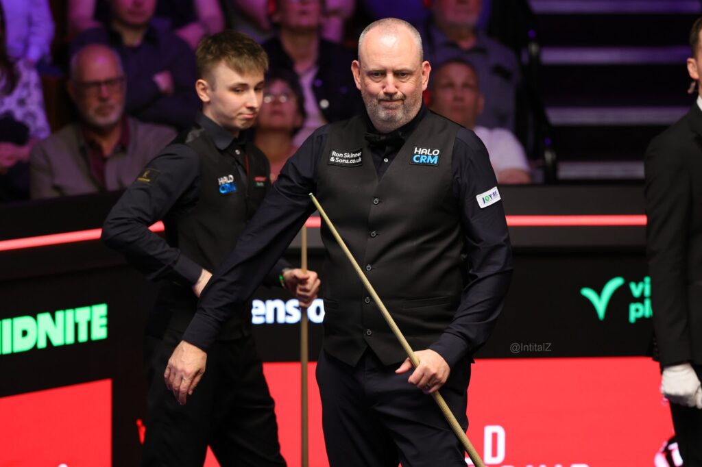 Mark Williams steht am Tisch und zieht ein Gesicht, Antoni Kowalski im Hintergrund.