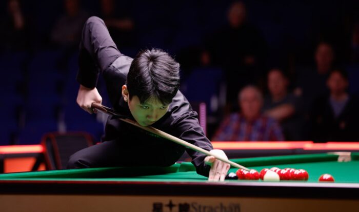 Während Runde 1 der Qualifikation hockt Lan Yuhao auf dem Tisch, er hat die Bockhand hoch aufgestellt, um über den schwarzen Ball die nächste Rote anzuvisieren.