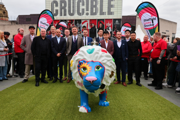 Vor dem Crucible Theatre und großen Wimpeln mit der Aufschrift:"Sheffield loves Snooker" posieren ein Großteil der Top16 auf dem grünen Teppich für ein Gruppenfoto mit der Weltmeisterschafts-Trophäe. Eine kindshohe blau-weiße und bunt bemalte Löwenstatue im Vordergrund stielt ihnen die Show.