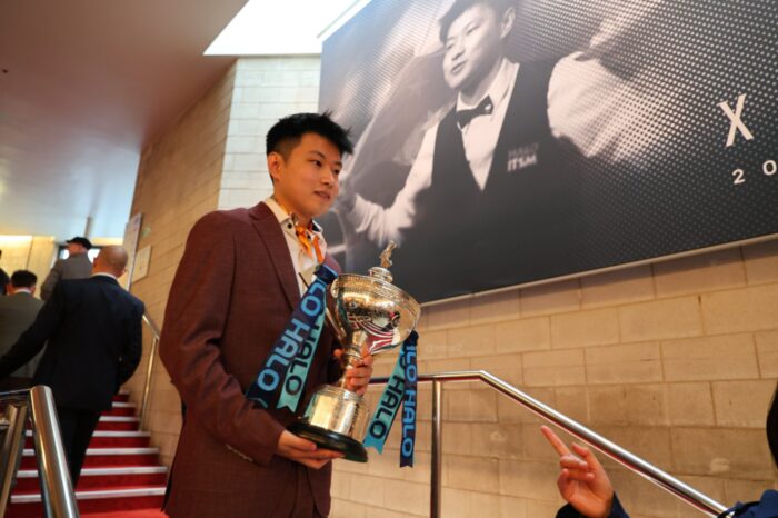 Zhao Xintong läuft vor seiner Titelverteidigung am Media Day mit dem WM-Pokal die Treppe im Crucible herunter.