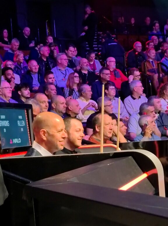 Barry Hawkins und Mark Allen lächelnd im Profil. Im Hintergrund Publikum.