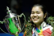 Panchaya Channoi mit WM-Titel, lächelnd, mit Pokal in Großaufnahme. Sie trägt einen Blumenkranz.