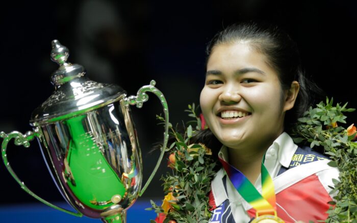 Panchaya Channoi mit WM-Titel, lächelnd, mit Pokal in Großaufnahme. Sie trägt einen Blumenkranz.