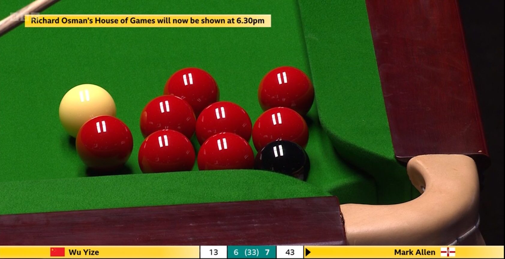 Beim Spielstand von 7 zu 6 für Mark Allen über Wu Yize steht es 43 zu 13 für Allen in Frame 14. Gezeigt ist eine Nahaufnahme der rechten Ecktasche an der Kopfbande, an die sich der Spielball sowie acht Rote kuscheln, der Eingang der Tasche wird dabei durch Schwarz blockiert. Oben im Bild sieht man einen Hinweis eingeblendet, dass sich die Ausstrahlung von Richard Osmans House of Games verzögert.