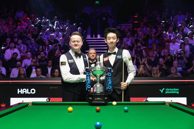 Shaun Murphy und Wu Yize vor dem Pokal der Weltmeisterschaft 2026. Hinter den beiden steht der Schiedsrichter Rob Spencer.