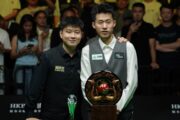 Zhao Xintong und Chang Bingyu posieren nach dem Finale der Wuhan Open 2026 für ein Foto. Vor Chang steht der Siegerpokal, ein verzierter Teller mit einer großen roten Kugel in der Mitte, umgeben von zwei Vögeln, vermutlich Pfauen.