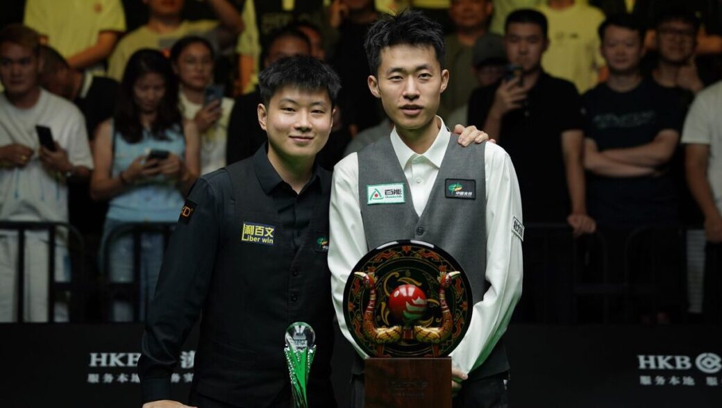 Zhao Xintong und Chang Bingyu posieren nach dem Finale der Wuhan Open 2026 für ein Foto. Vor Chang steht der Siegerpokal, ein verzierter Teller mit einer großen roten Kugel in der Mitte, umgeben von zwei Vögeln, vermutlich Pfauen.